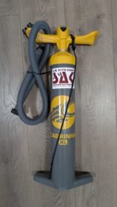 Cabrinha XL kite pump with yellow handle and gray cylindrical body, coiled hose, laid on wooden floor beside a blue rope. Specifically designed for inflating kites in kiteboarding adventures.