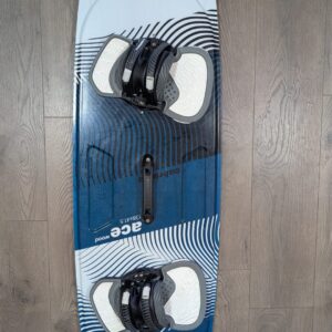 Blue and white wakeboard with black bindings mounted, lying on a wooden floor with circular graphic patterns on the board edges.