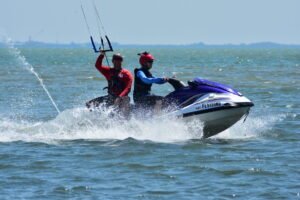 Two people on a purple Yamaha jet ski speed across choppy water, spraying waves, wearing helmets and life jackets.