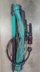 Kite control bar with teal lines wrapped around the bar and handles, stored on a wooden surface.